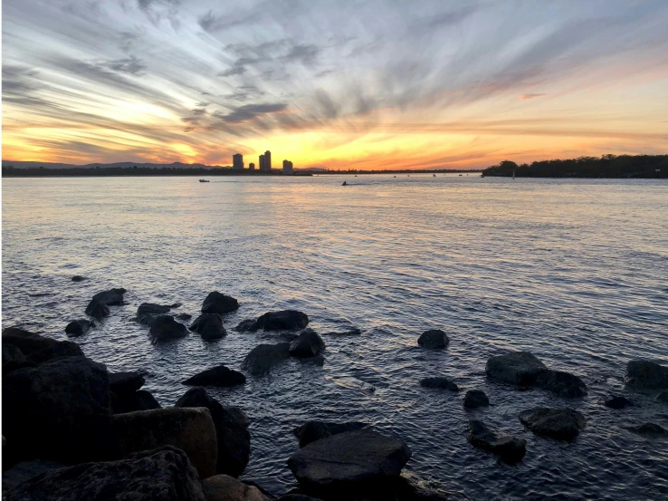 the sun sets over the water and rocks at the beach