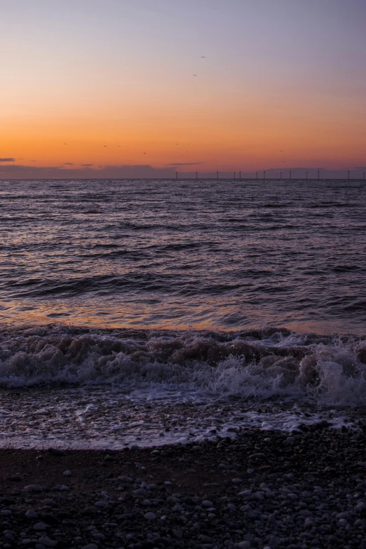 the sun rises over a calm ocean with sailboats