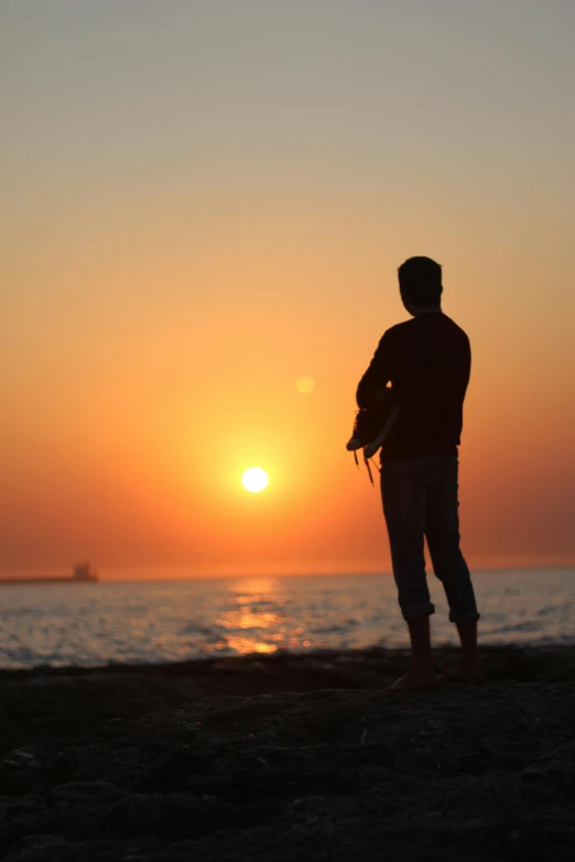 the silhouette of a man holding his surfboard at sunrise