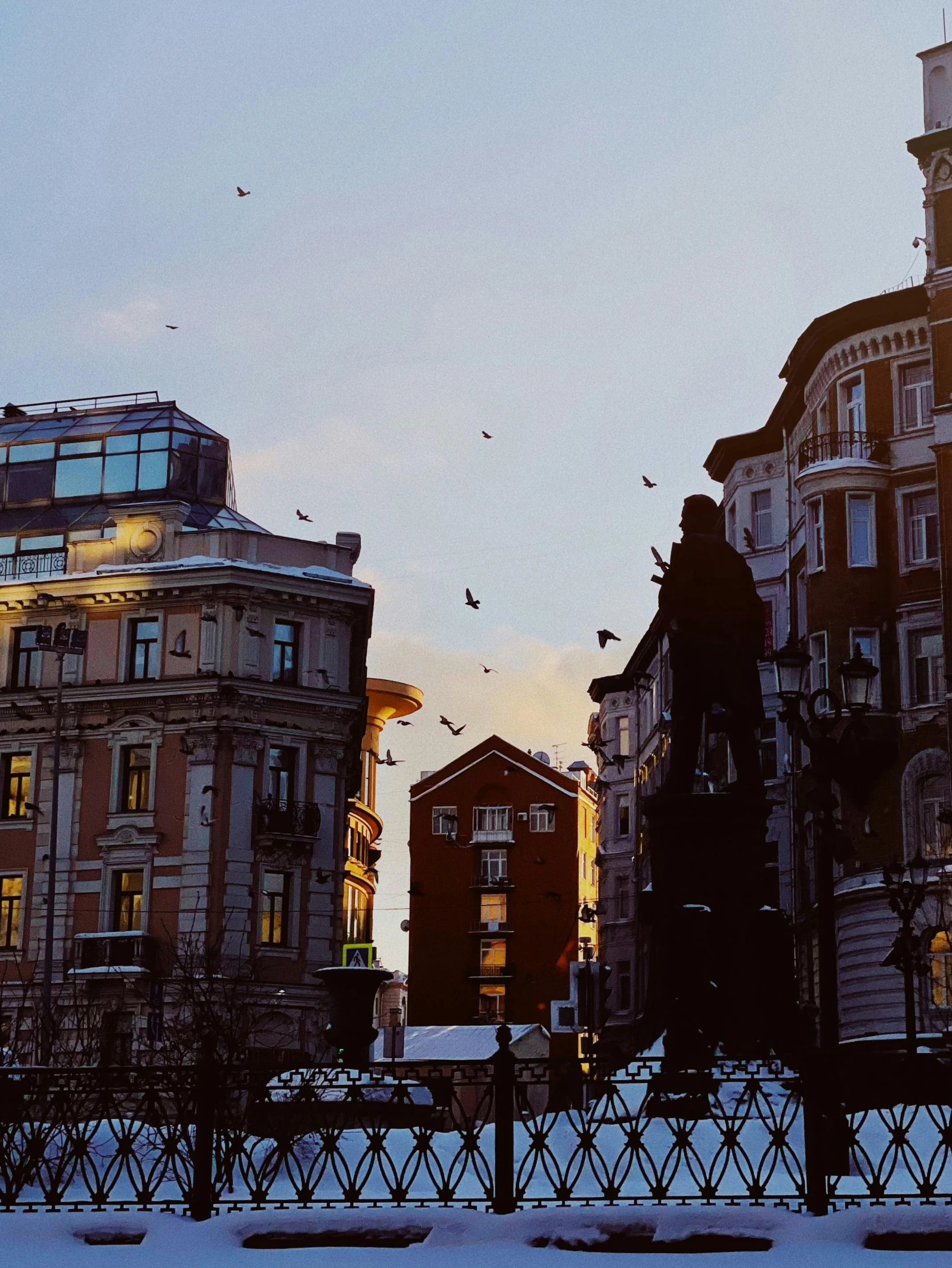 some birds flying over a city street with tall buildings