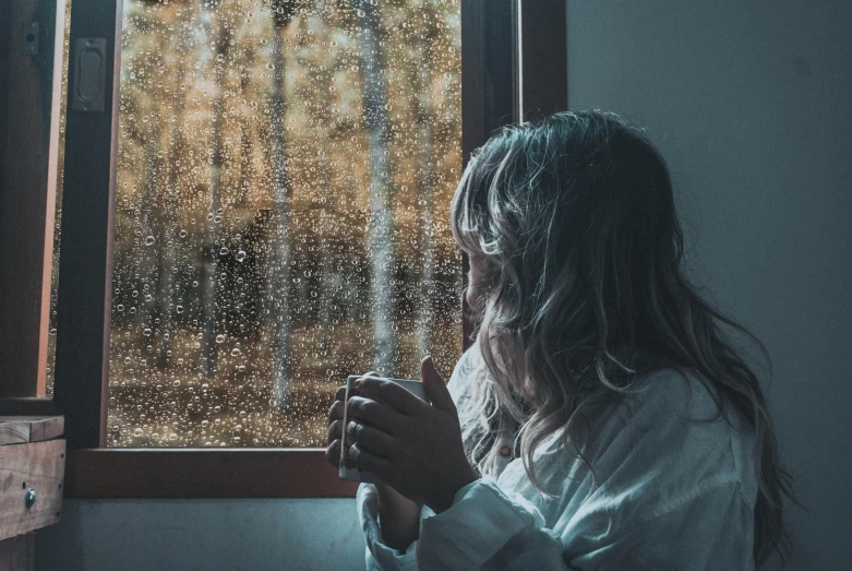 a woman stands behind a window with rainy glass on the outside