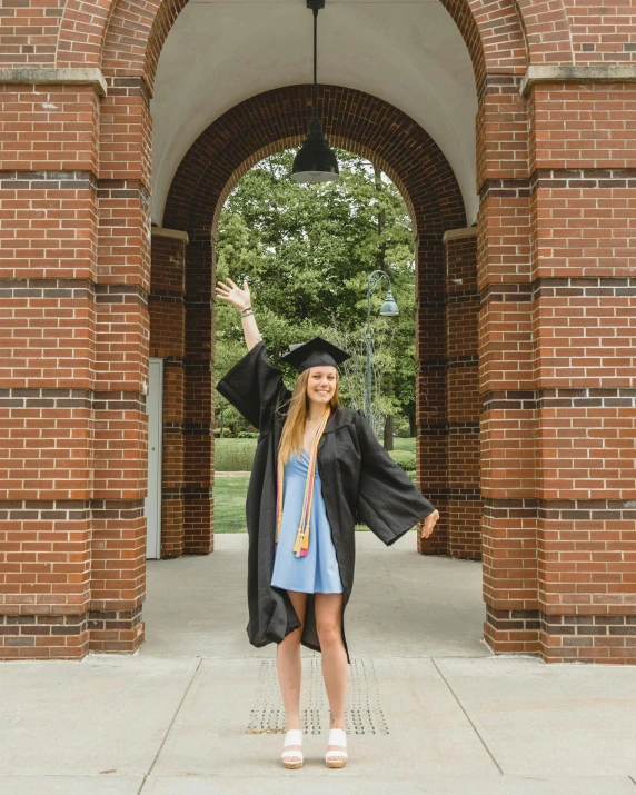 a girl in graduation dress standing in a brick archway with arms wide open