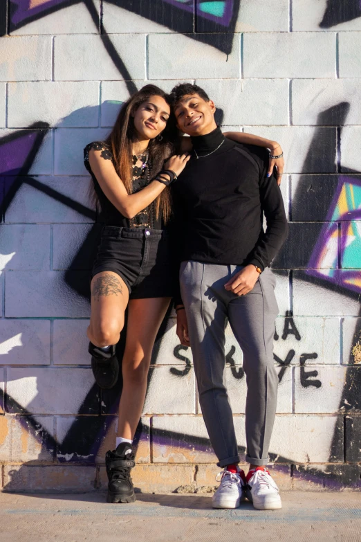 a young couple are standing in front of graffiti