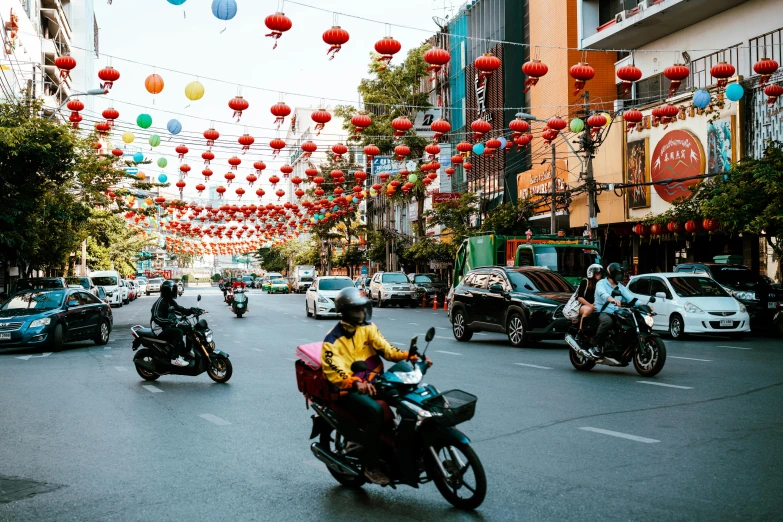 a street is full of motorcyclists and cars with decorations hanging above them
