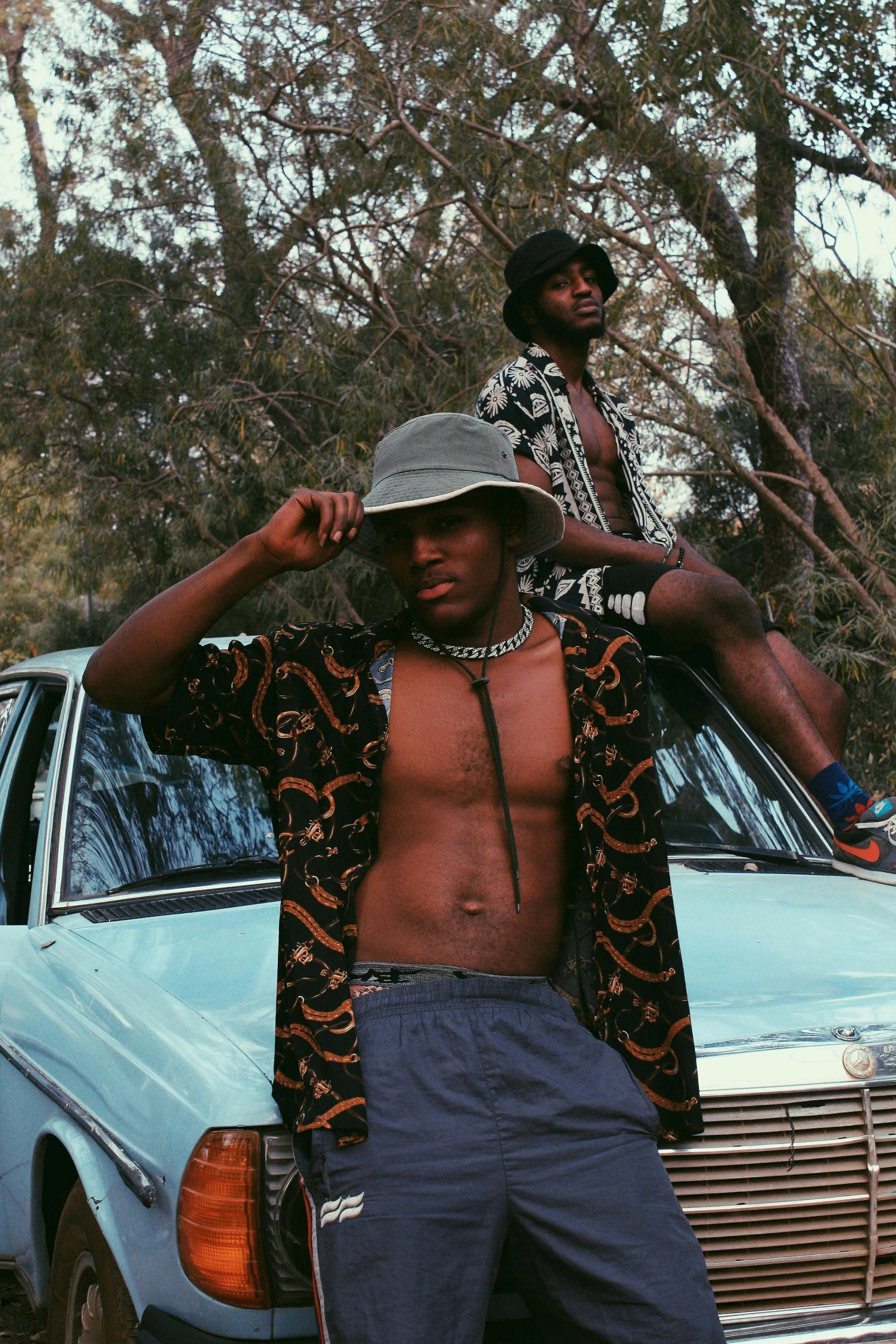 a man is standing by the car and another one is showing off his shirt