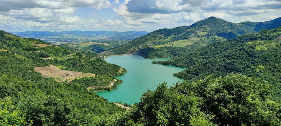 a lake and trees on the mountain with cloudy skies