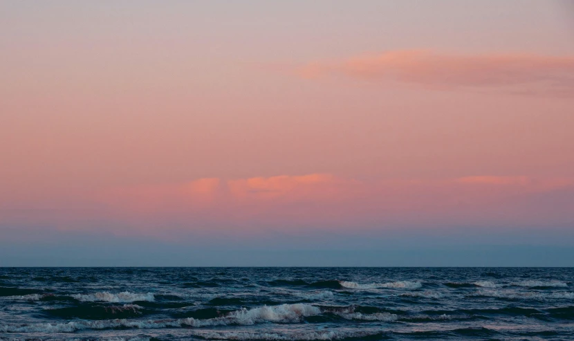 people are para sailing in the water under a pink sky