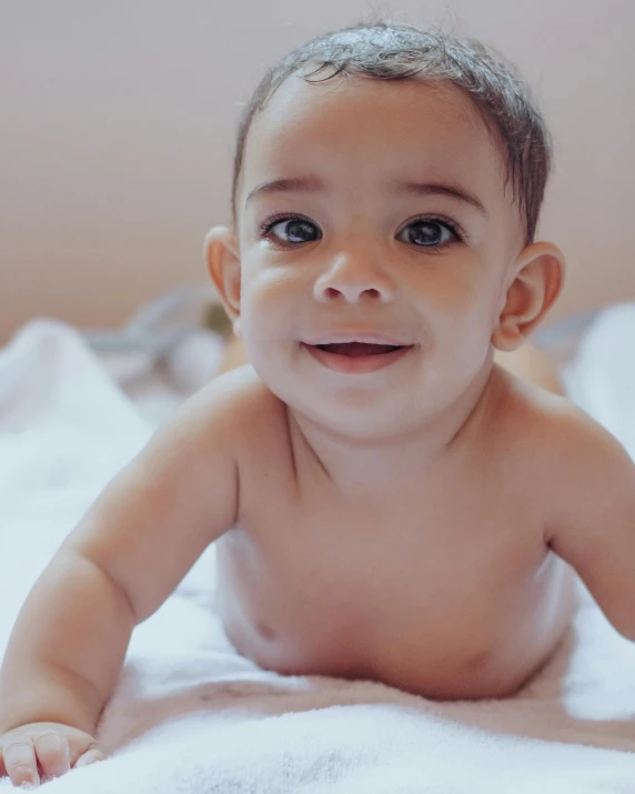 a  baby with light hair and blue eyes laying on a bed