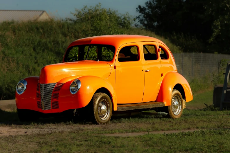 an orange vintage car in the grass with trees