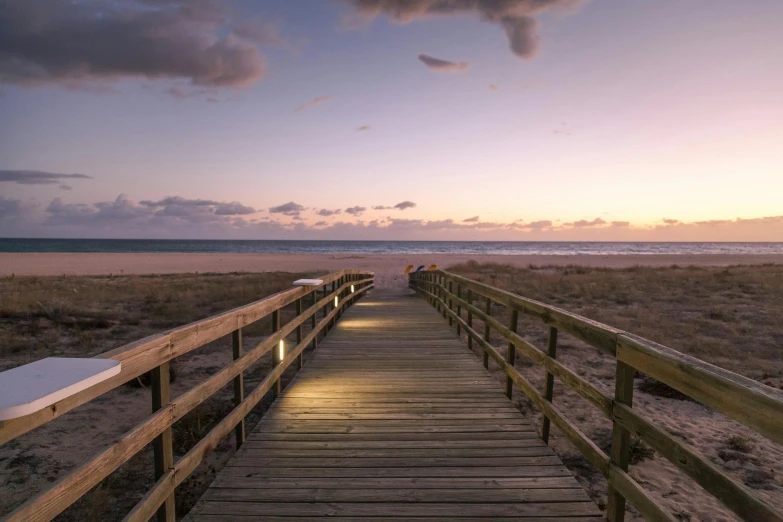 a boardwalk that leads to the beach with benches under the boardwalk