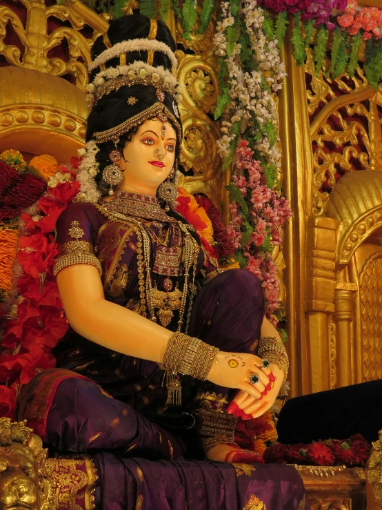 an indian woman sits in front of flowers and gold