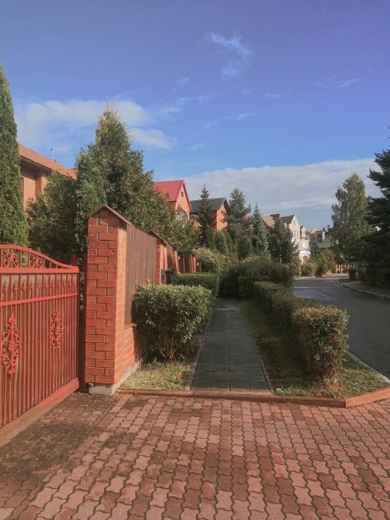 the red gate is in front of the brick sidewalk and a street