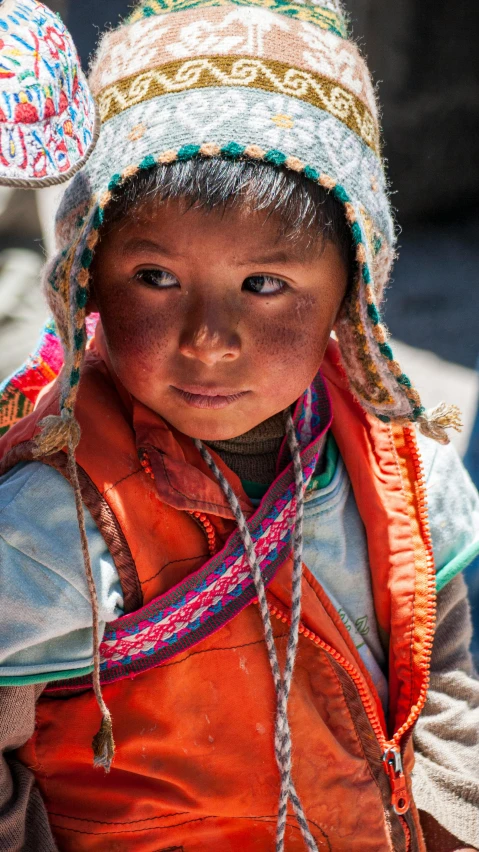 an indian girl wearing an orange vest and a colorful hat