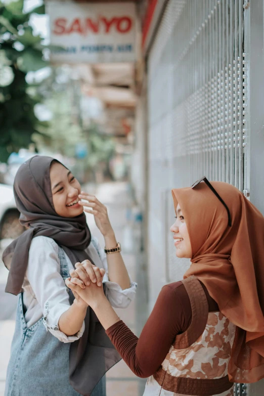 two woman shake hands against a wall near a sign