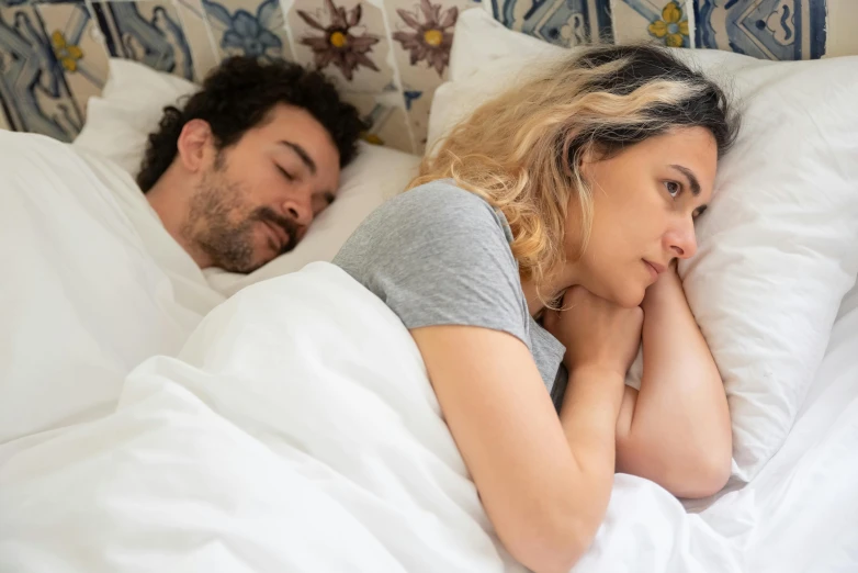 a man laying in bed with a woman who is sleeping next to her