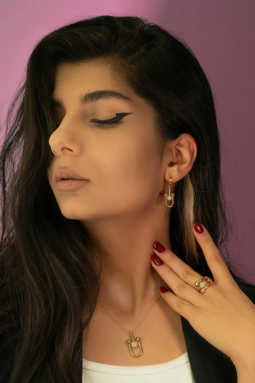 a woman standing in front of a pink wall wearing large earrings