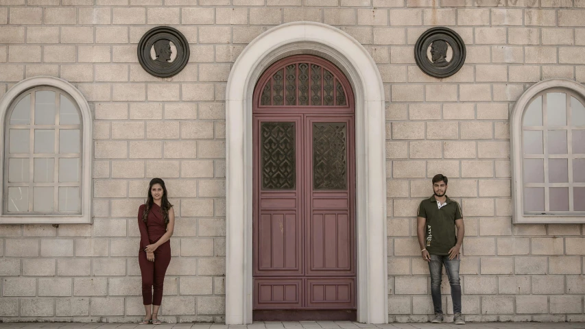 a young man and woman standing by a stone building with red doors