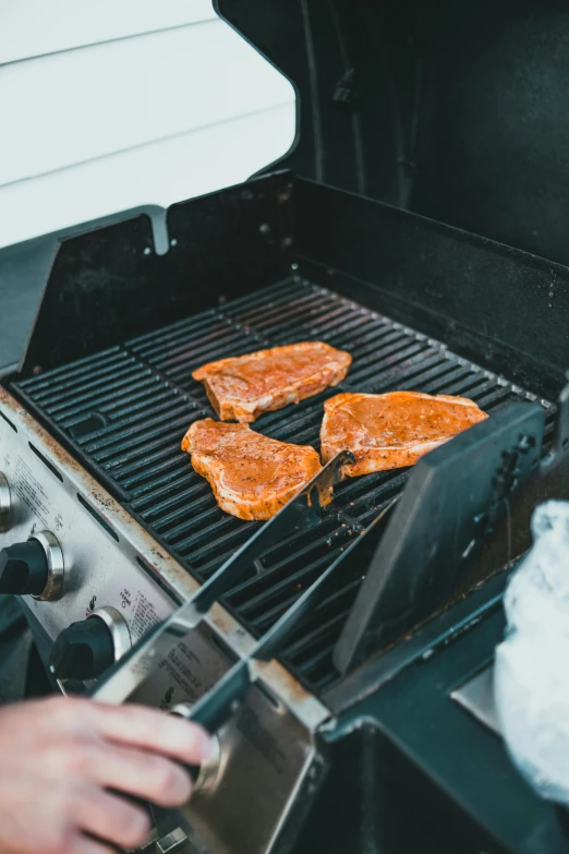 an outdoor grill with four pieces of meat being put on it