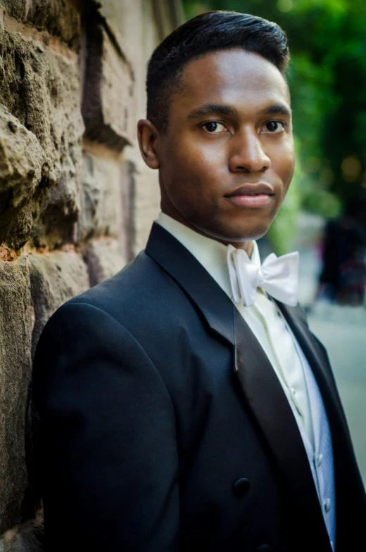 man in tuxedo standing against a stone wall