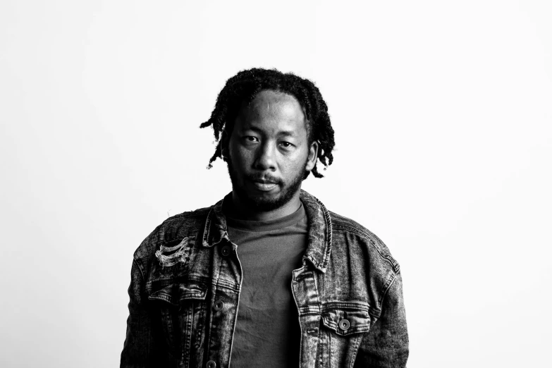 a man in denim jacket standing up against a white wall