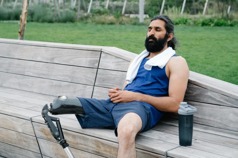 a man with an injured arm and leg ce sits on a wooden bench in a park