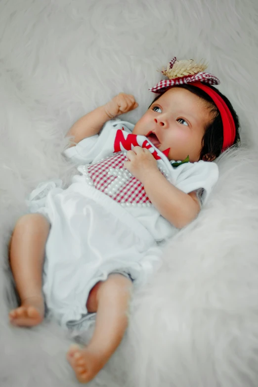 an infant girl with her hair tied in a red and white checkered ribbon laying on a fluffy white sheet