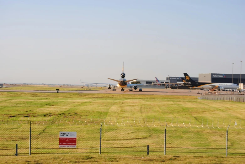 two airplanes sit on the runway near a wire fence