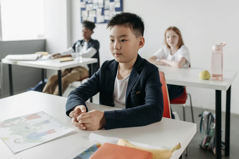 a group of children are sitting in classroom chairs with notebooks on them