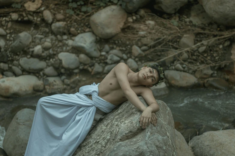 a man in a white gown laying on a rock