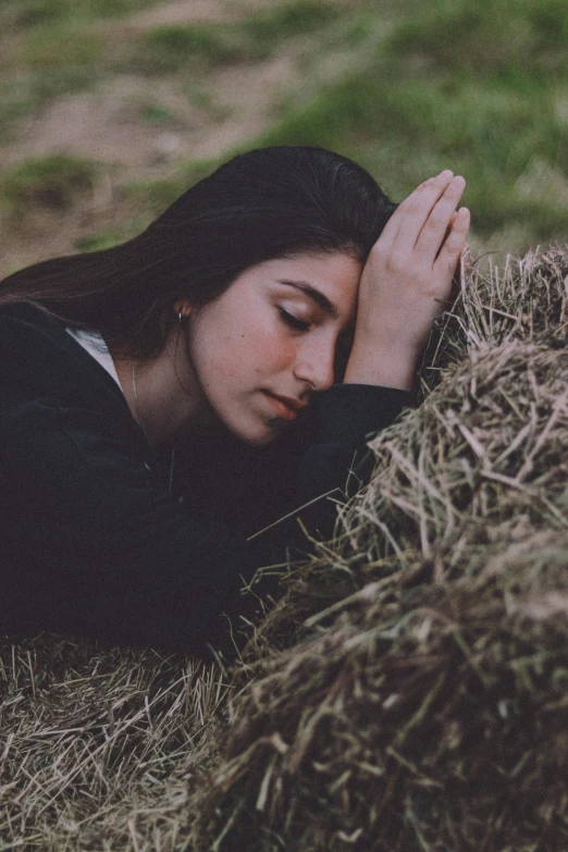 a woman laying in the grass next to a pile of hay