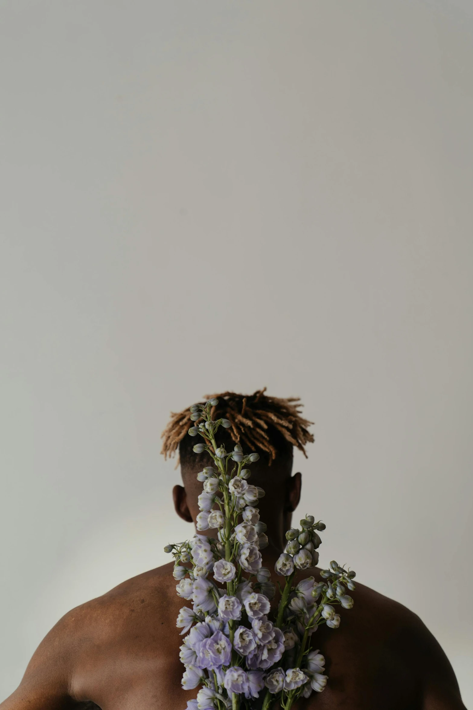 a man is standing against a white wall and has purple flowers in his hair