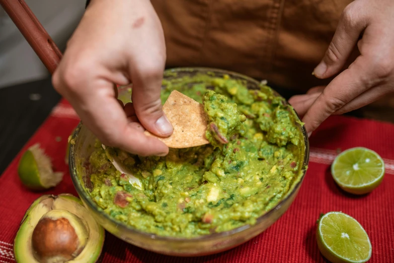 someone dipping guacamole in an old glass bowl with lime wedges