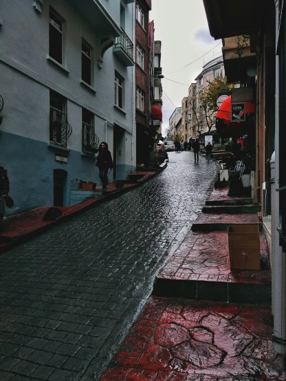 red tiles on the ground are beside gray buildings and an umbrella is hanging over a city street