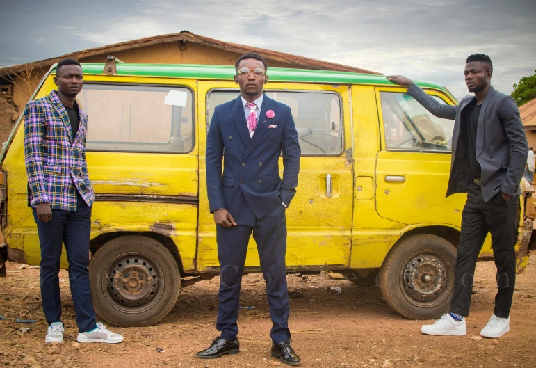 three black men stand next to a yellow van