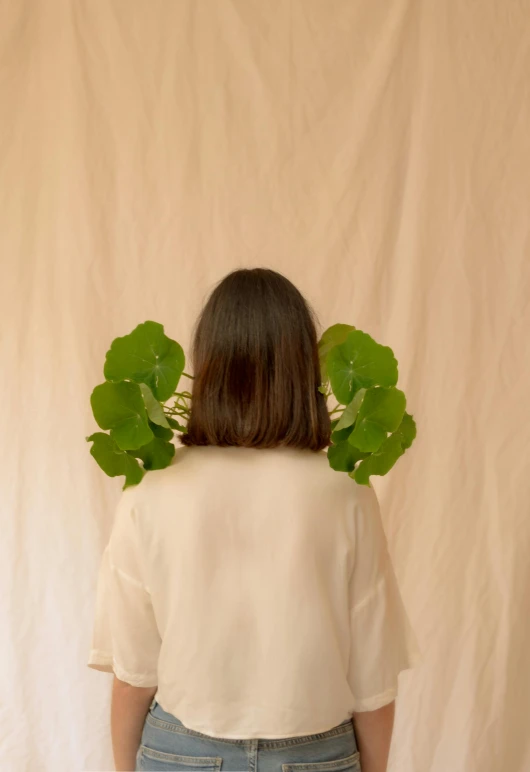 the back of a woman standing in front of a wall holding green leaves