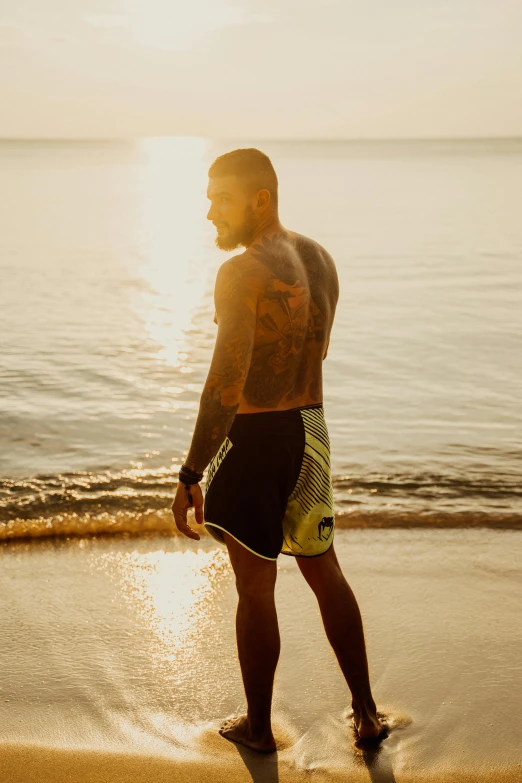 a man in the sunset walking into the water on the beach