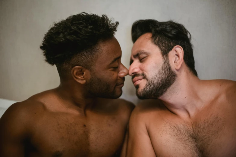 two shirtless men lie side by side in bed