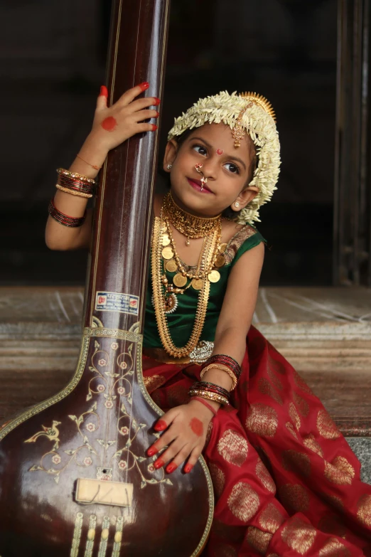 a little girl sitting on the ground holding onto a guitar