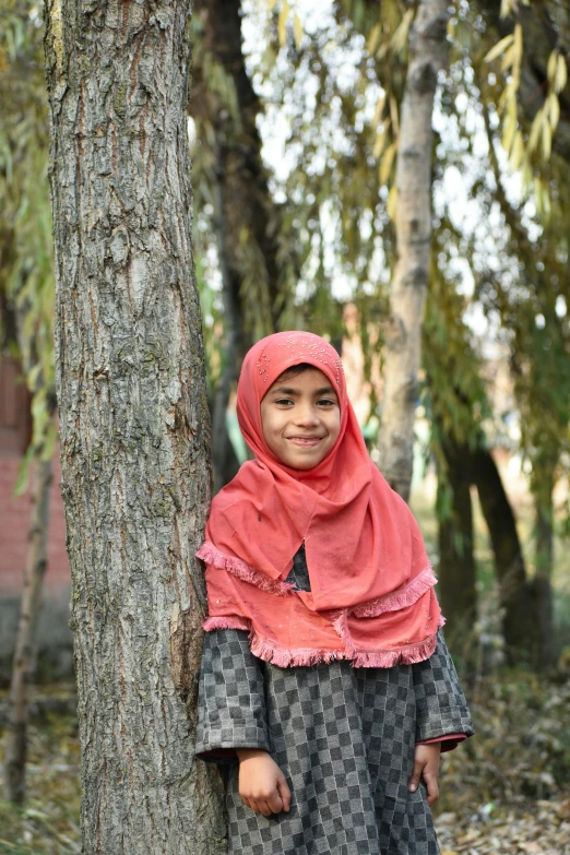 a little girl in a shawl posing against a tree