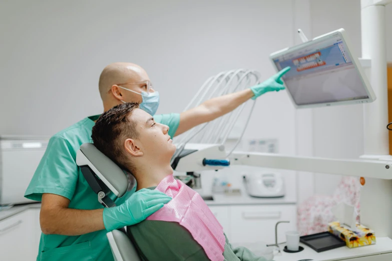 man in green scrubs sitting in a dentist chair while another person uses a computer