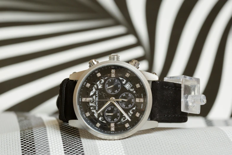 an analog watch sits on the surface with a black and white stripe wall behind it