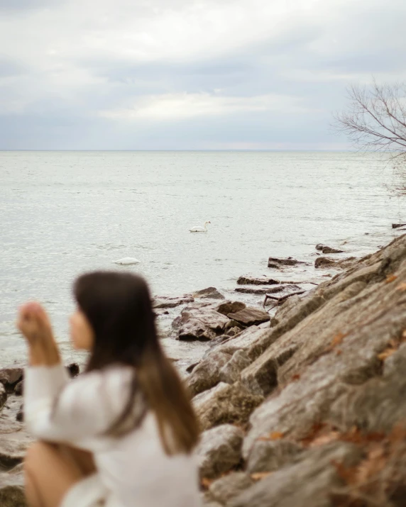 a woman on rocks watching water with a bird flying over her head