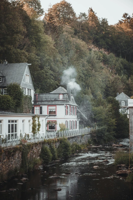 the view from across a small river shows houses, a bridge and a steam rising out of their windows