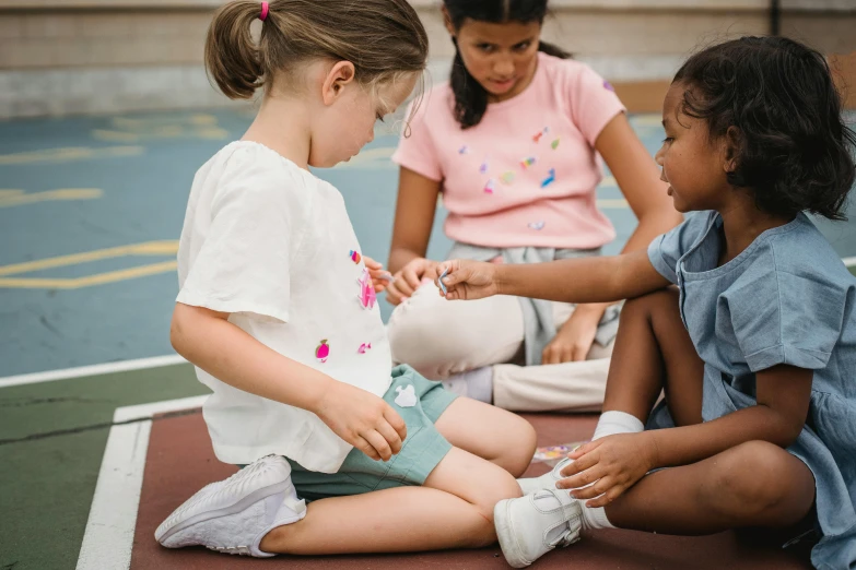 two girls and one boy play on a court while one girl sits on the ground