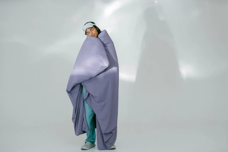 a woman is wrapped up in a blanket while standing against a wall