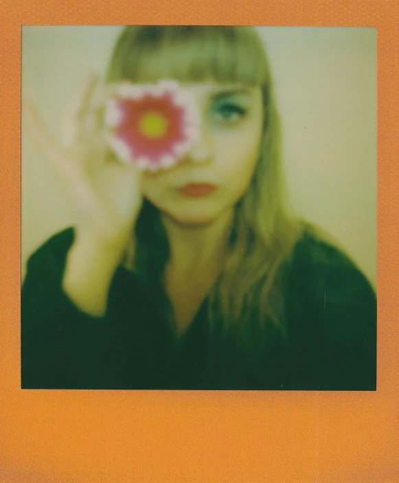 a woman looking through a polaroid with a flower on it's cheek