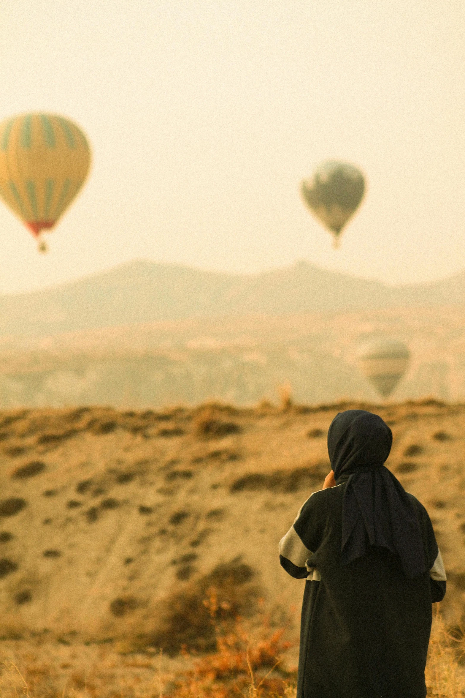 a girl in a hoodie looking out at  air balloons