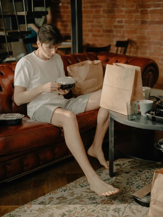 a young man sitting on a couch holding a cup in his hand