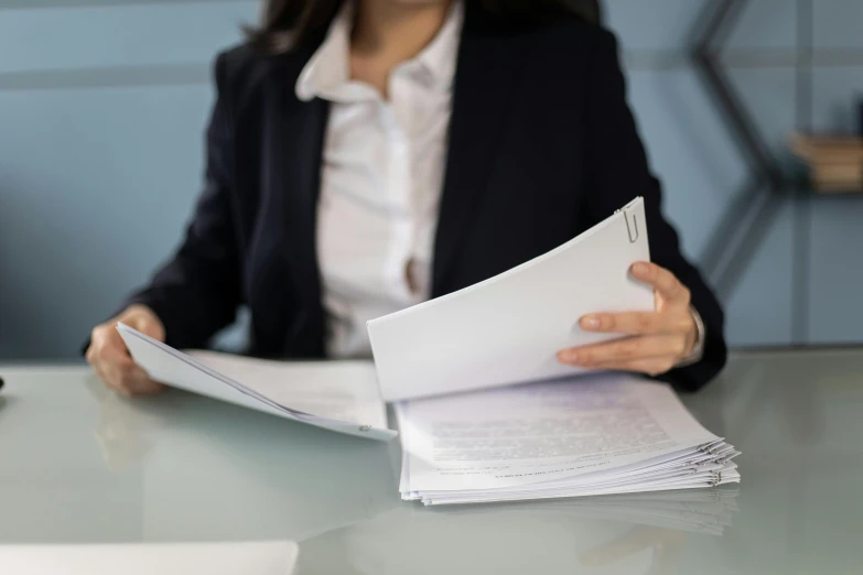 woman holding files and sitting at table in front of computer