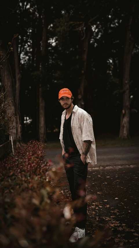 a man in black pants and an orange cap standing in a leafy area